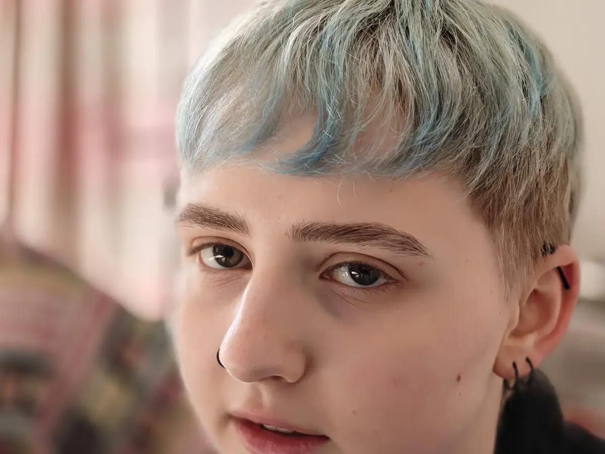 Portraitfoto von Moony, blau-blonde Haare, weiße Hautfarbe, Piercings in Nase und Ohr